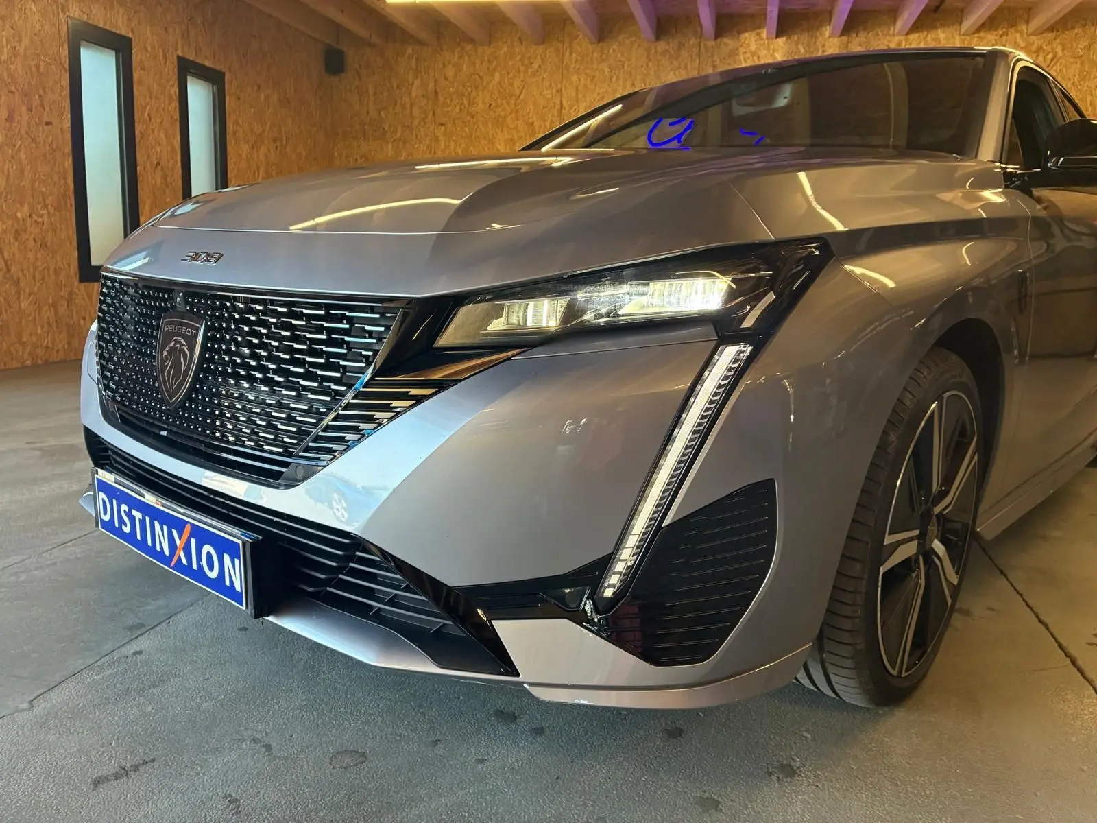 Vue 3/4 avant droit d'une Peugeot 308 gris métallisé avec calandre noire et feux LED distinctifs, en intérieur.