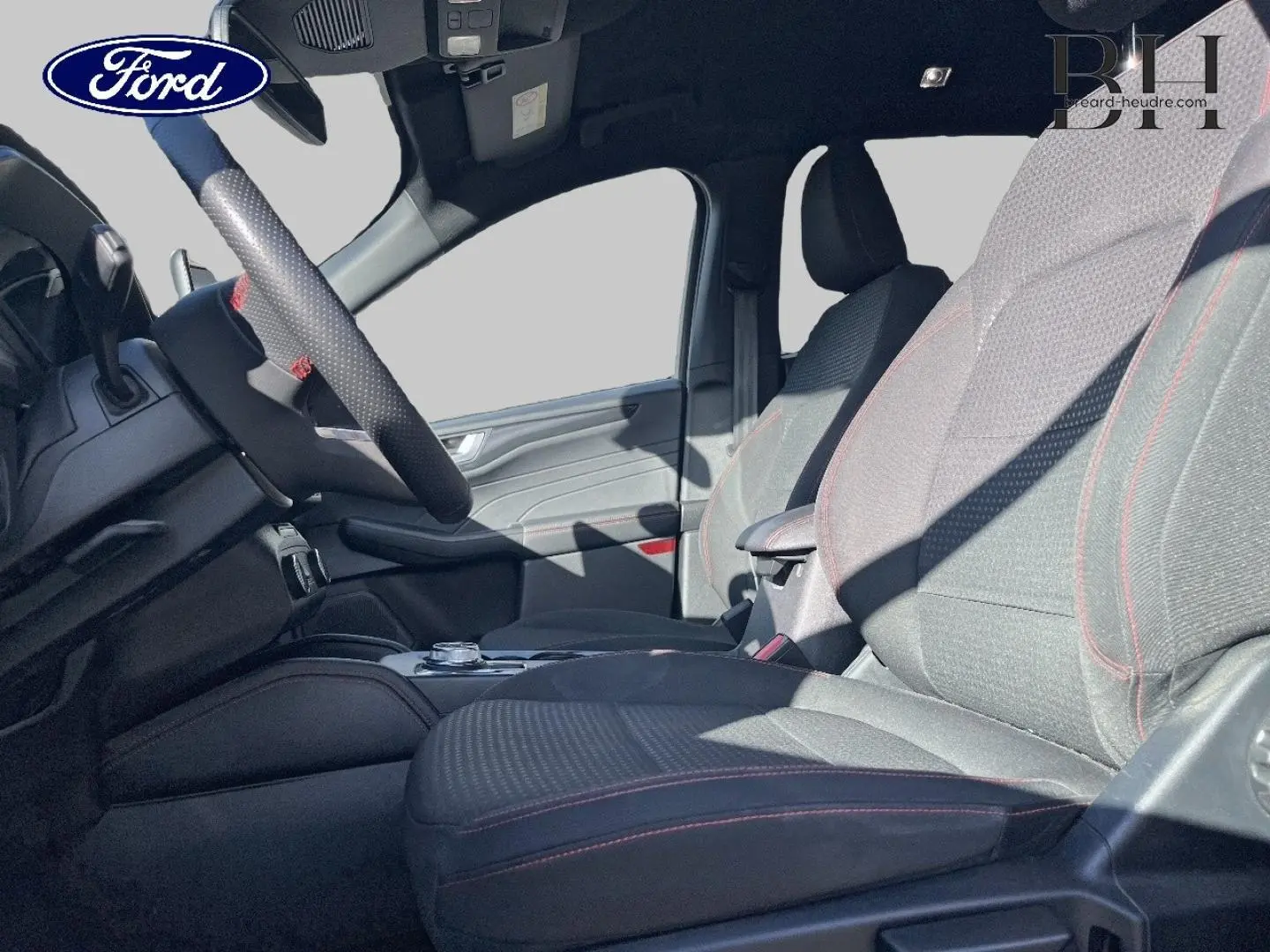 Vue intérieure côté gauche du Ford Kuga 2023, sièges sport noirs avec surpiqûres rouges et volant cuir multifonction.