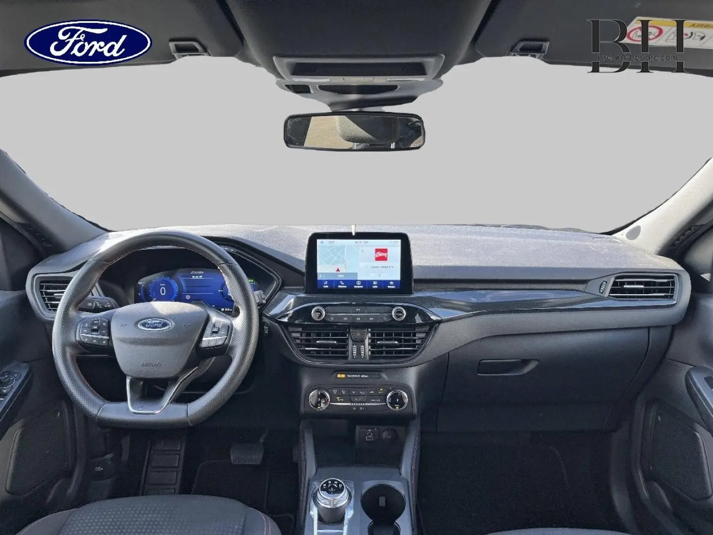 Vue frontale de l'intérieur du Ford Kuga 2023, tableau de bord noir avec écran tactile central et volant multifonction cuir.