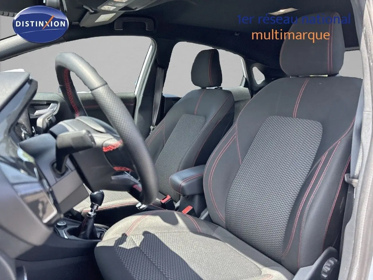 Intérieur avant du Ford Puma blanc 2022, sièges noirs avec surpiqûres rouges et volant cuir perforé avec coutures rouges.