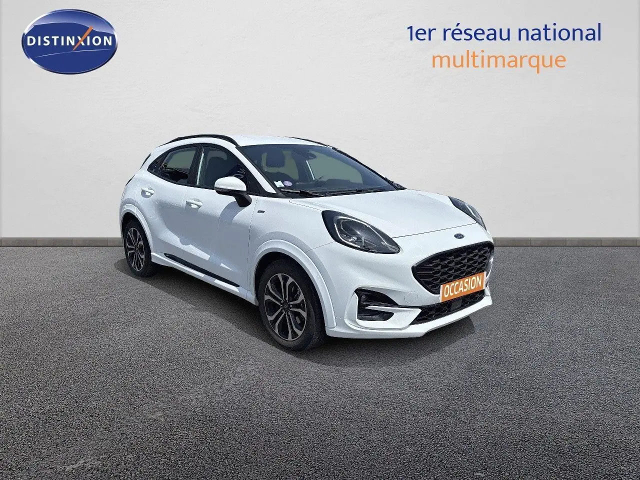 Ford Puma blanc en 3/4 avant droit avec calandre noire et jantes alliage, stationné devant un mur gris.