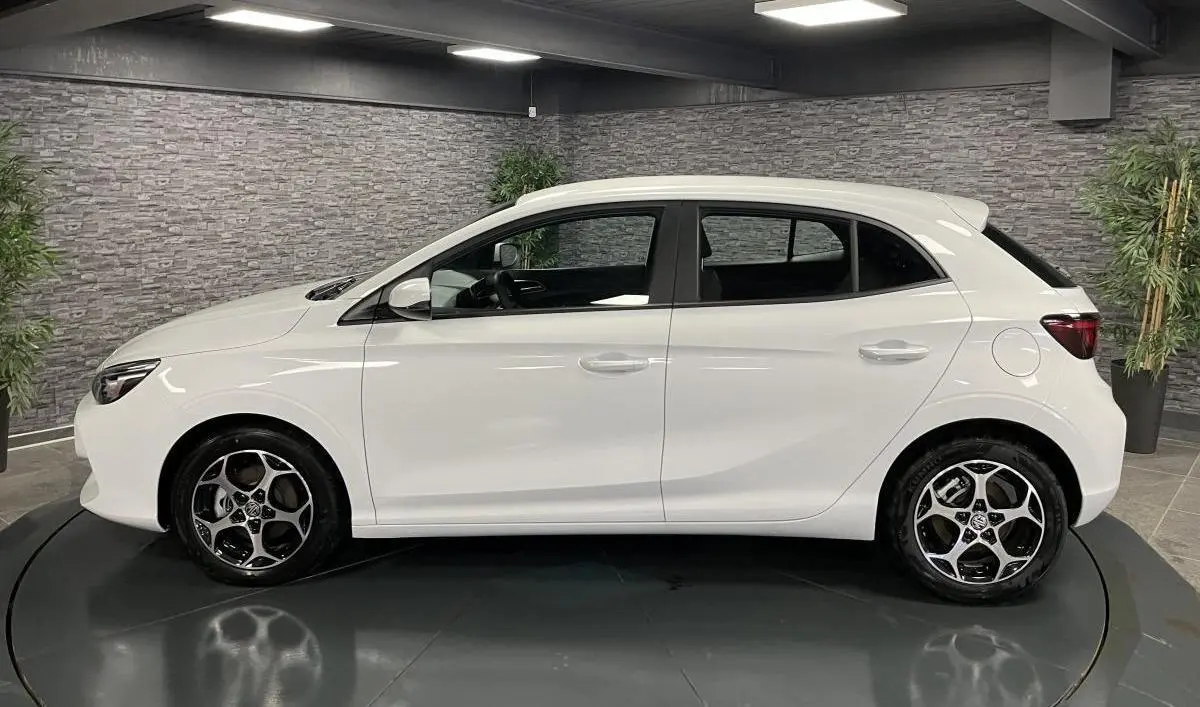 Vue latérale droite d'une MG3 1.5 Hybrid+ 195 Comfort blanche avec jantes alliage 16 pouces dans un showroom.