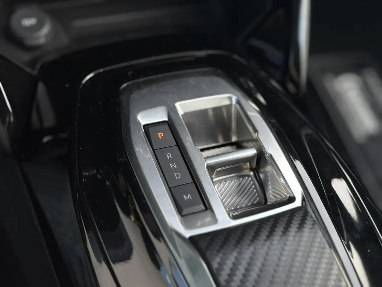 Gros plan sur la console centrale noire brillante du Peugeot 2008 Hybrid 145 avec sélecteur de boîte automatique.