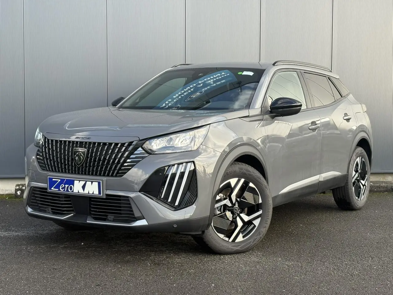 Peugeot 2008 Hybrid 145 e-DSC6 Allure gris Selenium en 3/4 avant droit avec jantes alliage bi-ton et barres de toit noires.