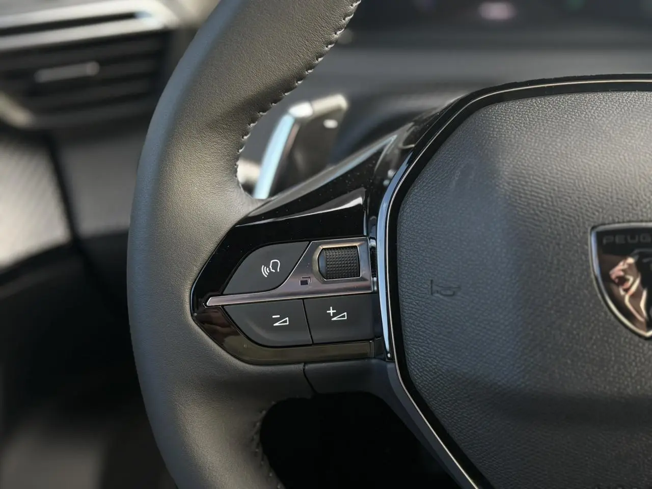 Gros plan sur le volant cuir noir du Peugeot 2008 Hybrid 145 e-DSC6 Allure avec commandes multimédia intégrées.