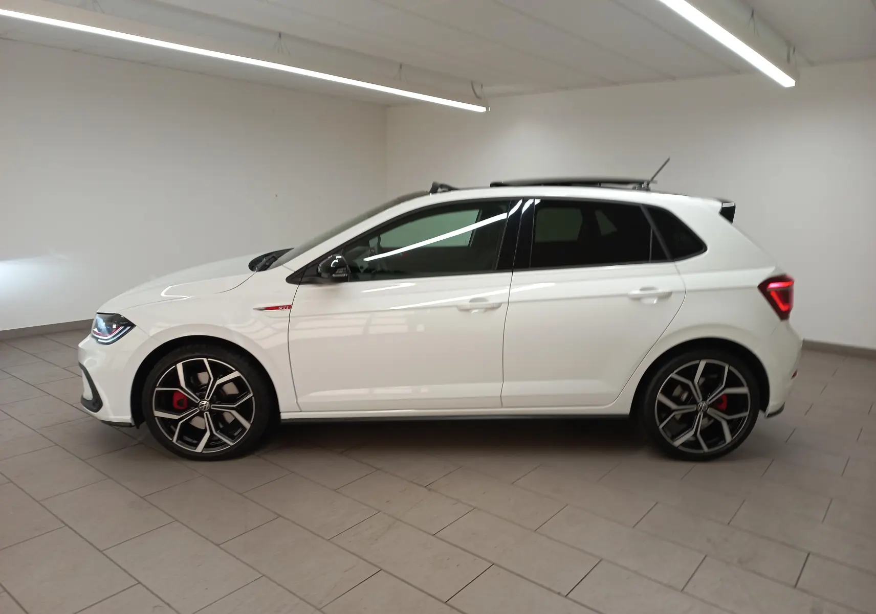 Vue de profil côté gauche d'une Volkswagen Polo GTI 2024 blanc pur avec toit noir et jantes sport noires et rouges.