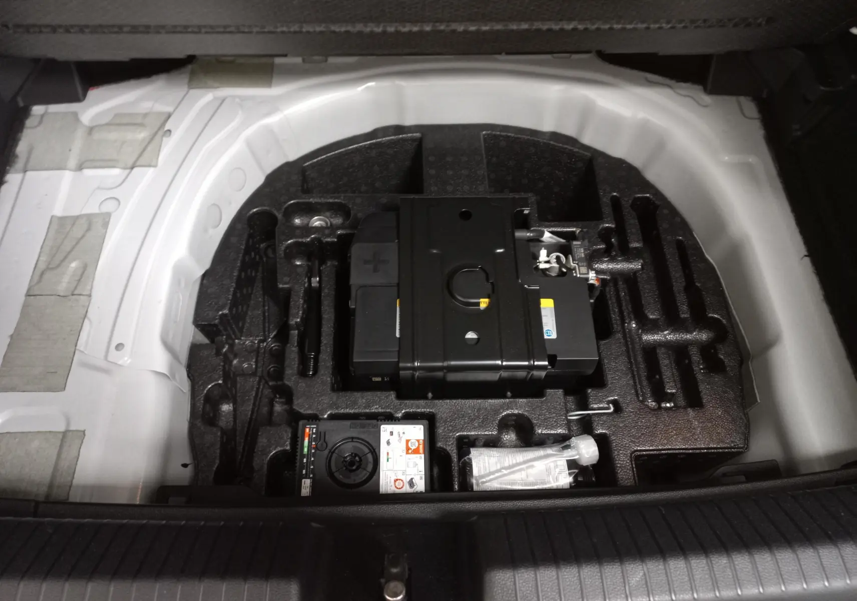 Coffre ouvert montrant le rangement sous plancher avec batterie et outils du Volkswagen Polo 2.0 TSI blanc toit noir 2024.