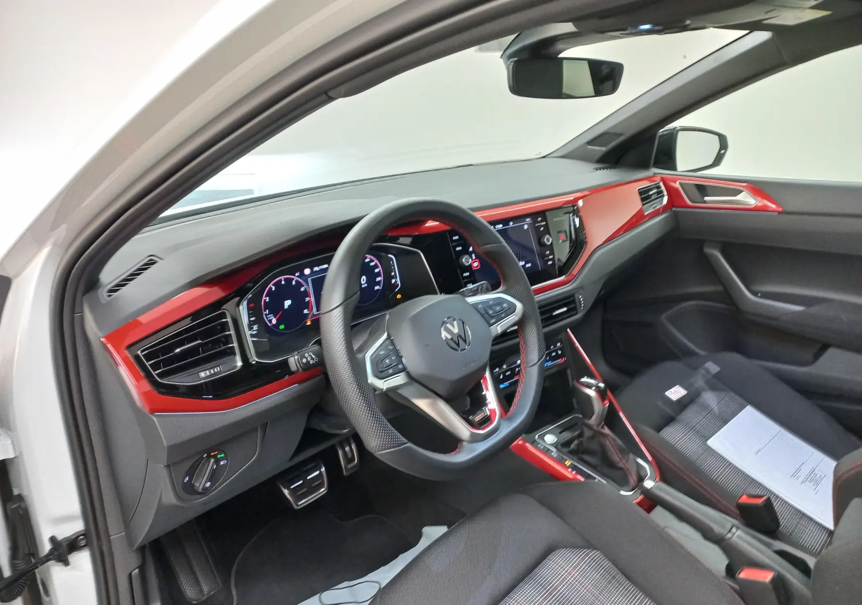 Vue intérieure côté conducteur de la Volkswagen Polo 2024 avec tableau de bord rouge et volant multifonction noir.