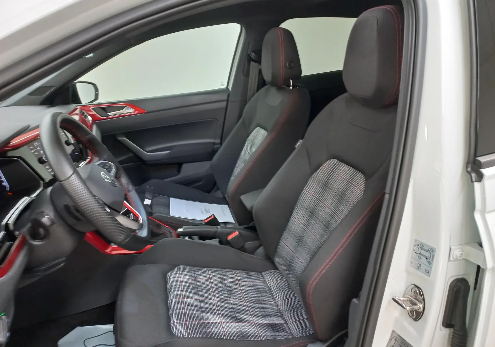 Vue intérieure côté conducteur de la Volkswagen Polo GTI 2024, sièges tissu à motif écossais avec surpiqûres rouges.