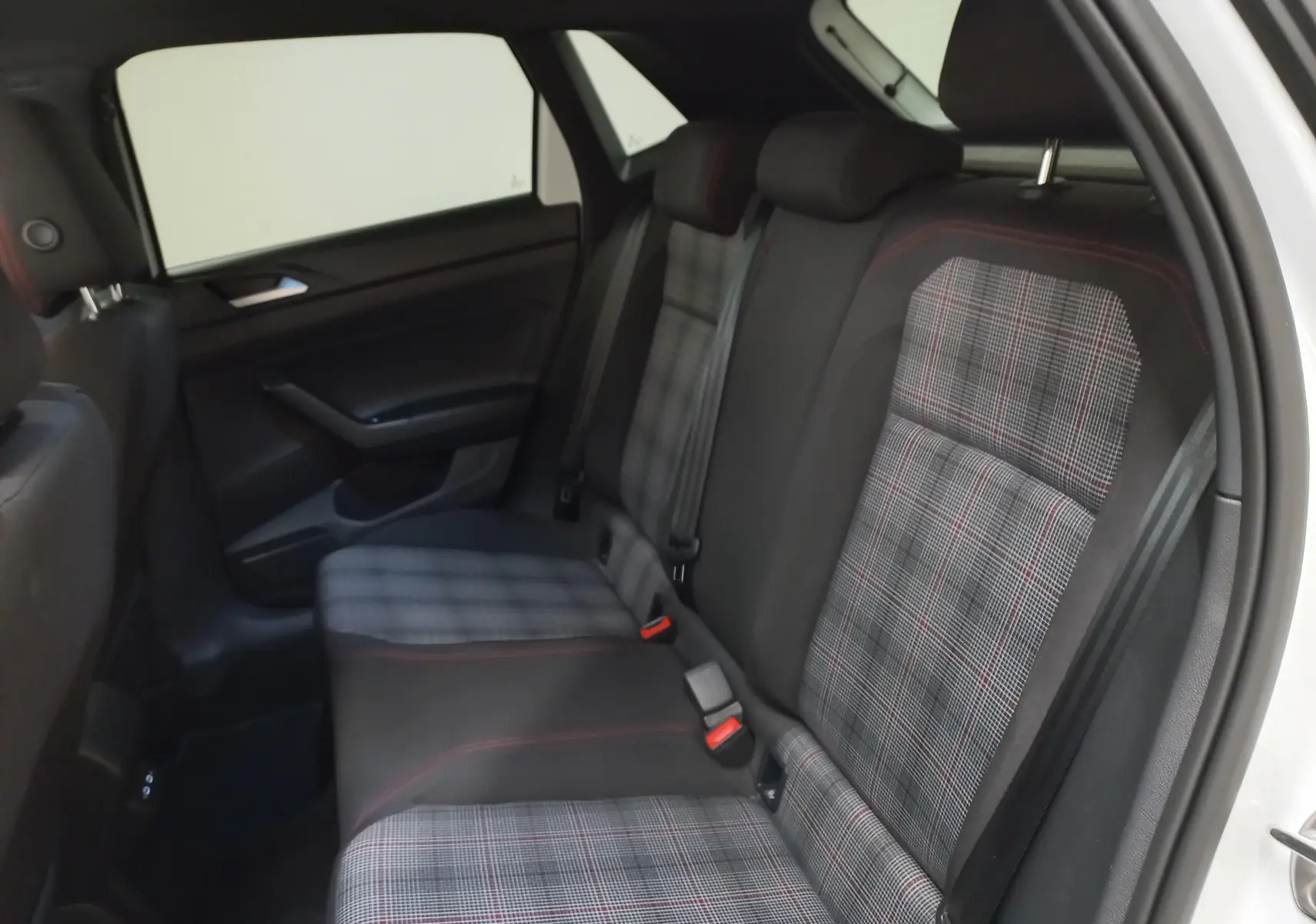Vue intérieure côté droit des sièges arrière à motif tartan gris avec surpiqûres rouges dans une Volkswagen Polo GTI 2024 blanc pur toit noir.