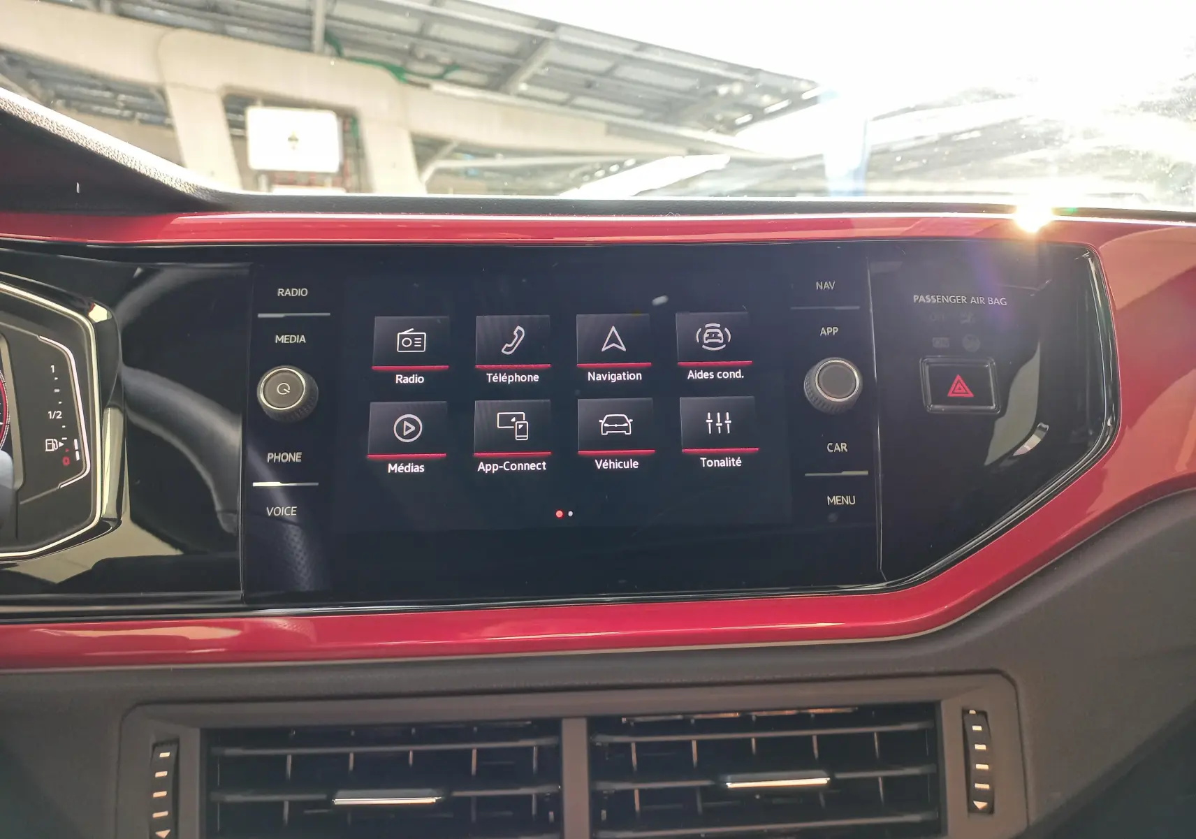 Vue rapprochée de l'écran tactile central rouge et noir du tableau de bord de la Volkswagen Polo 2024 GTI avec interface multimédia affichée.