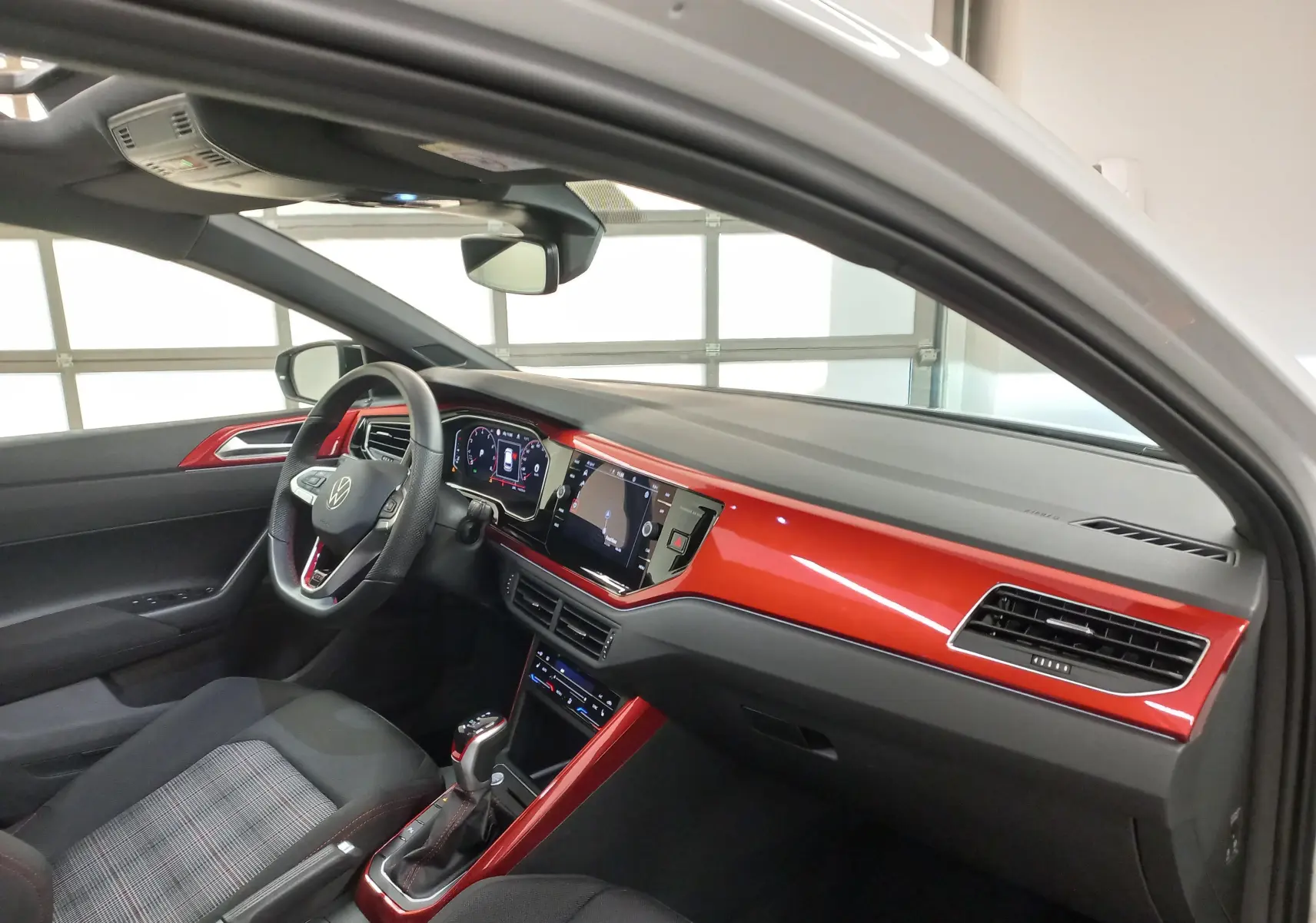 Vue intérieure côté conducteur de la Volkswagen Polo 2024 GTI avec tableau de bord rouge brillant et sièges tissu à motif.