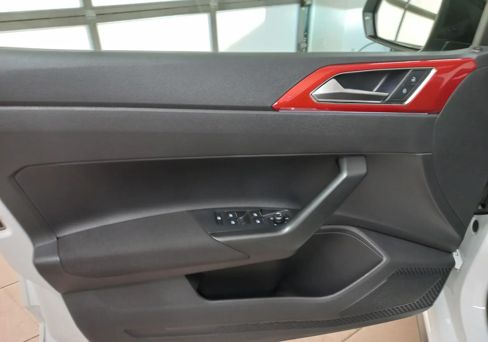 Gros plan sur la porte avant gauche de la Volkswagen Polo 2024, avec insert rouge brillant et commandes de vitres noires.