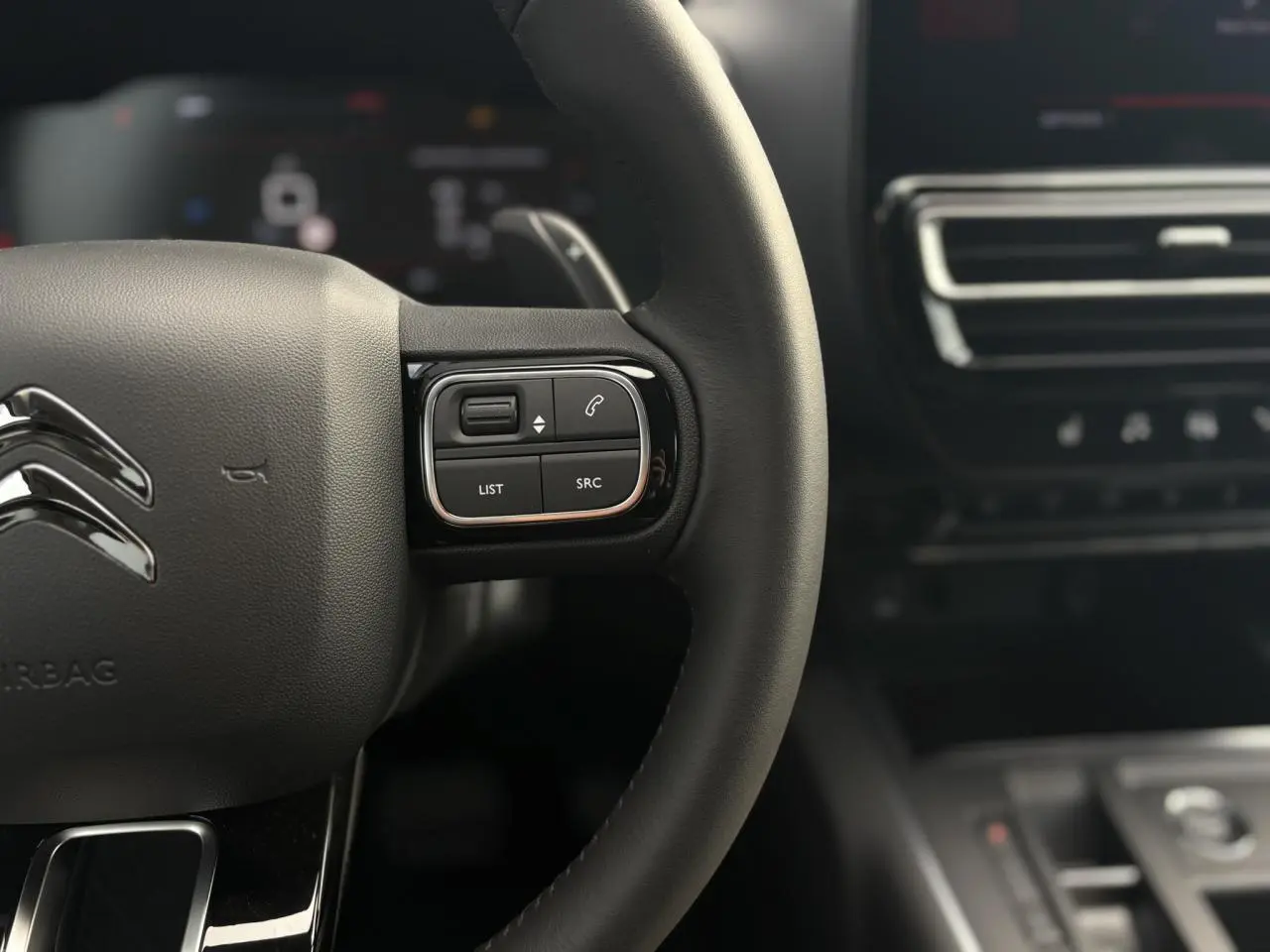 Gros plan sur le volant noir du Citroën C5 Aircross 2025 avec commandes intégrées et tableau de bord flou en arrière-plan.