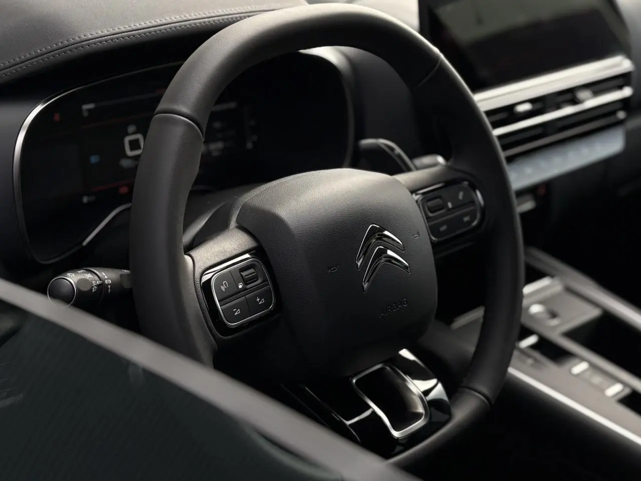 Gros plan sur le volant noir du Citroën C5 Aircross 2025 avec commandes intégrées et tableau de bord numérique flou en arrière-plan.