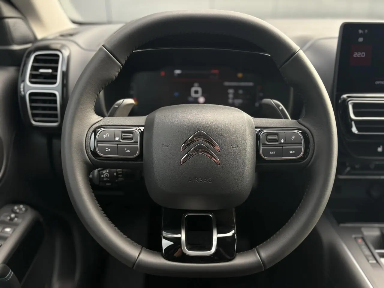 Vue rapprochée du volant en cuir noir du Citroën C5 Aircross 2025 avec commandes intégrées et tableau de bord numérique flou.