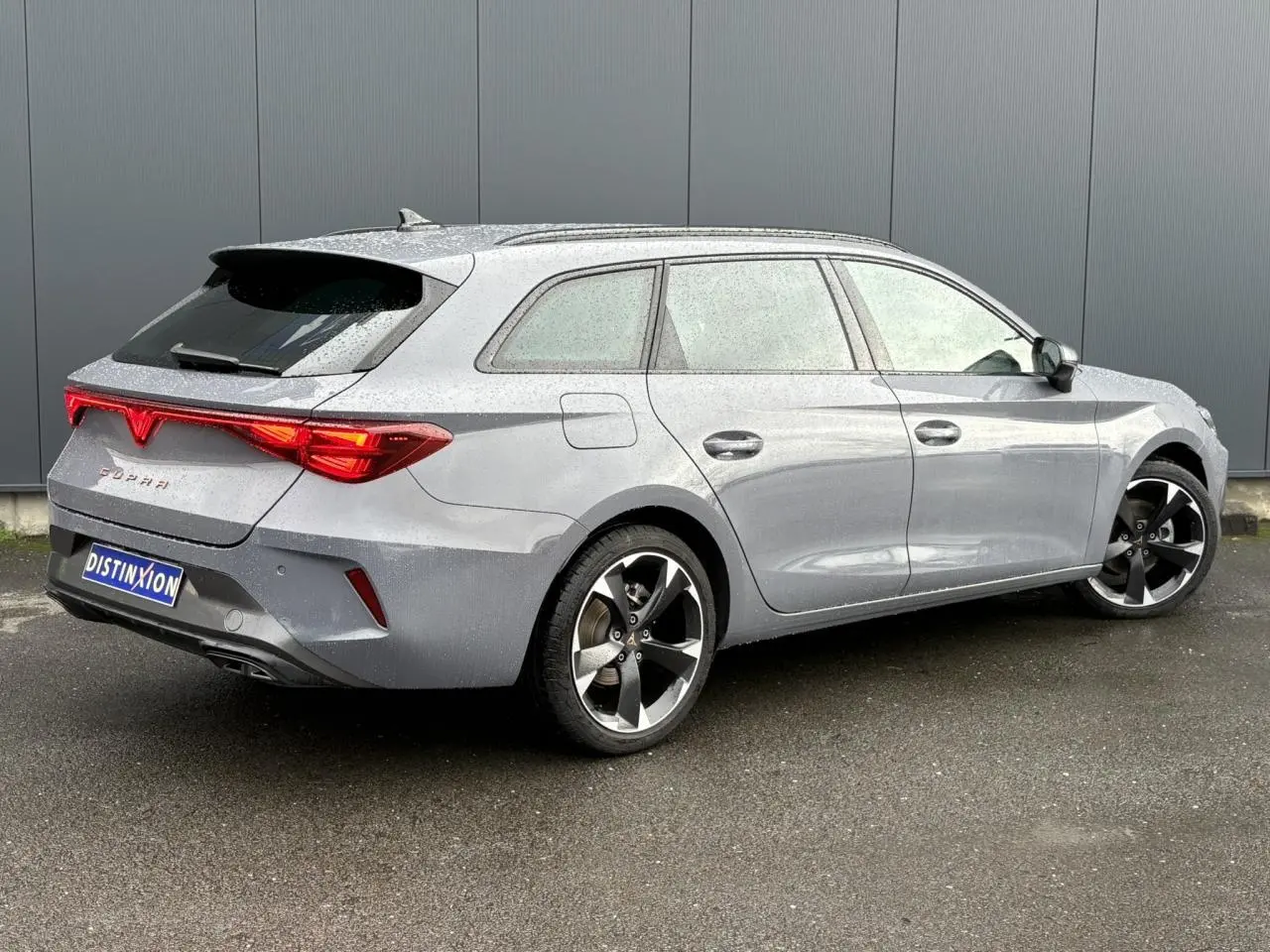 Vue 3/4 arrière droite d'une CUPRA Leon ST 1.5 e-TSI gris Graphene avec feux arrière Tri-LED et jantes alliage 18 pouces.