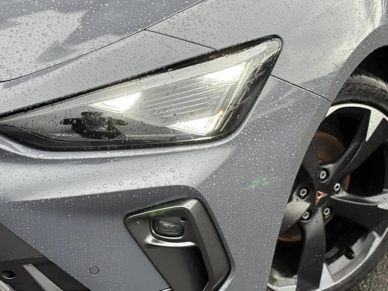 Gros plan sur l'avant droit gris Graphene d'une CUPRA LEON ST 2025, avec phare LED allumé et jante alliage noire.
