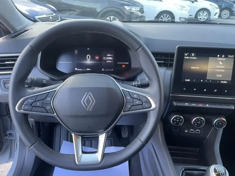 Vue intérieure centrée sur le volant de la Renault Clio V gris métal, avec tableau de bord numérique et écran tactile.