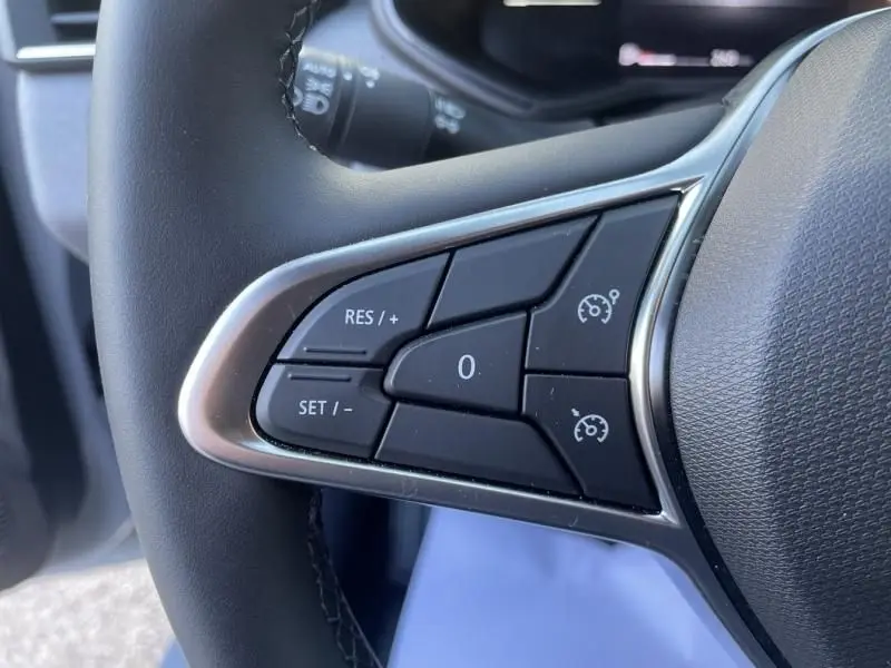 Gros plan sur les commandes au volant à gauche de la Renault Clio V DCI 100 Evolution gris métal, boutons de régulateur de vitesse.