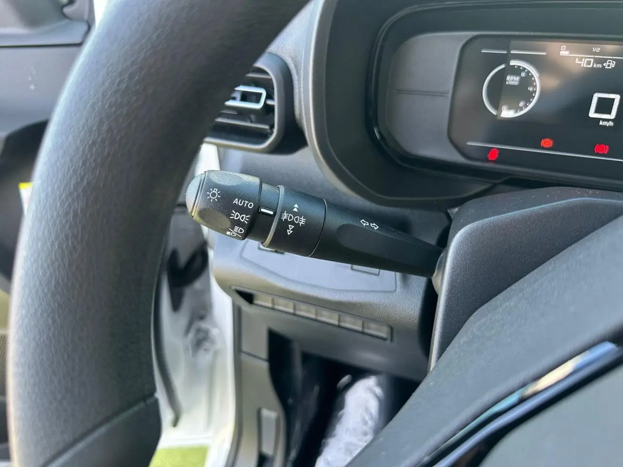 Gros plan sur la manette de commandes d’éclairage à gauche du volant d’un Citroën Berlingo blanc, tableau de bord numérique visible.