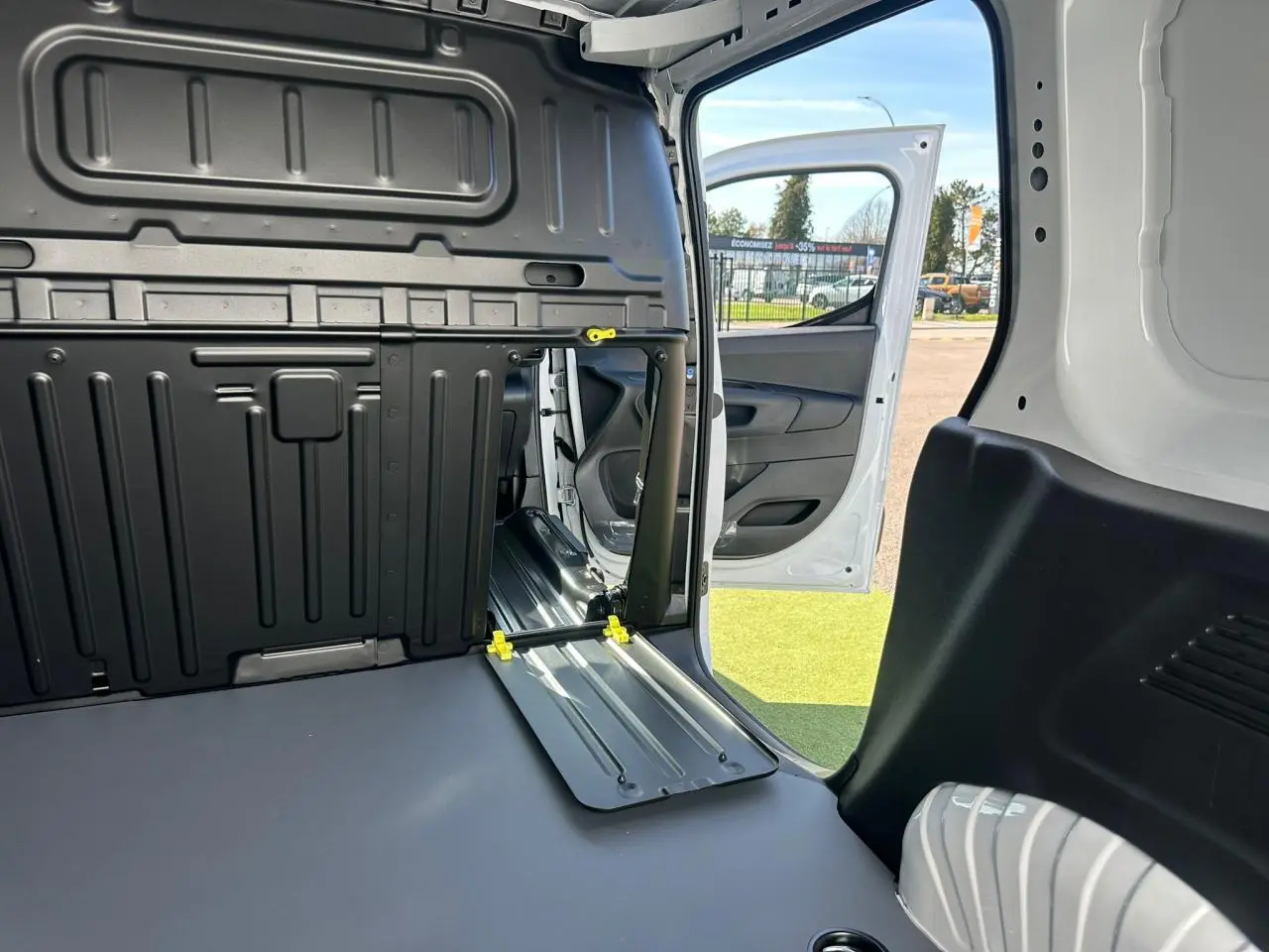 Vue rapprochée de l'espace entre les sièges arrière noirs du Citroën Berlingo III blanc, avec console centrale basse.
