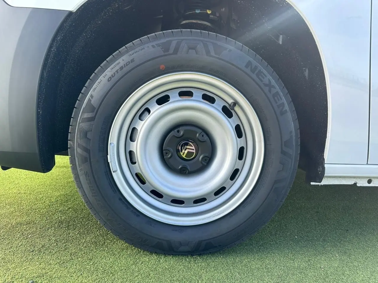 Gros plan sur la roue arrière droite en jante tôle grise du Citroën Berlingo blanc Icy, partie basse de la carrosserie visible.