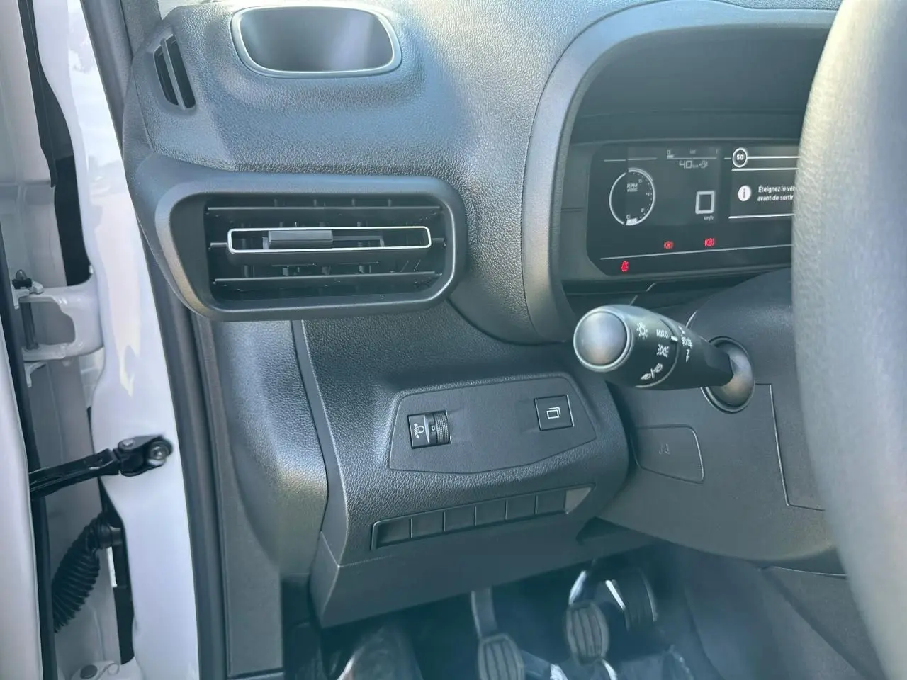 Vue rapprochée côté gauche du tableau de bord noir avec commandes d'éclairage et pédales du Citroën Berlingo blanc Icy.