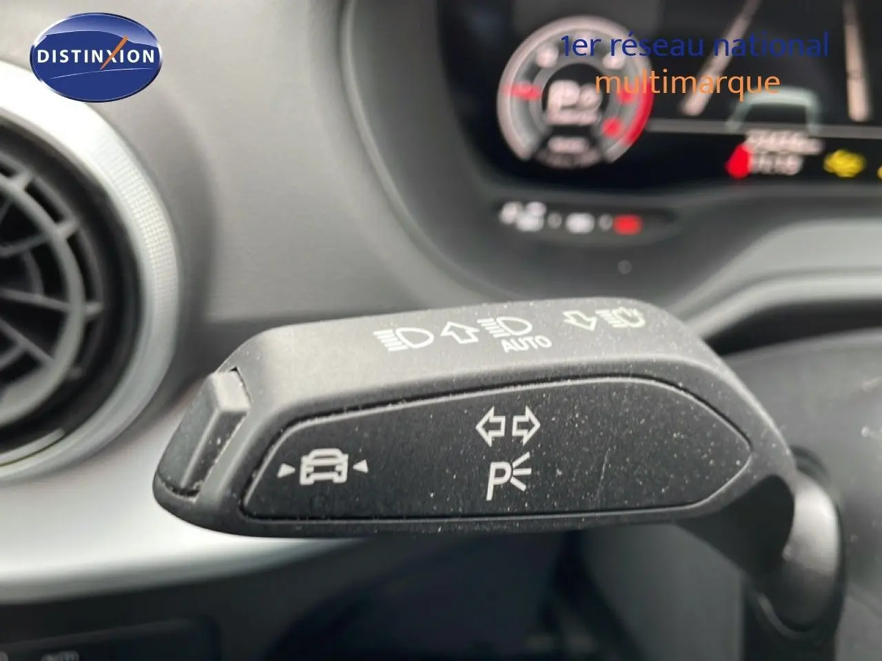 Gros plan sur la commande de clignotant et feux d’un Audi Q2 noir mito metal, intérieur avec tableau de bord flou en arrière-plan.