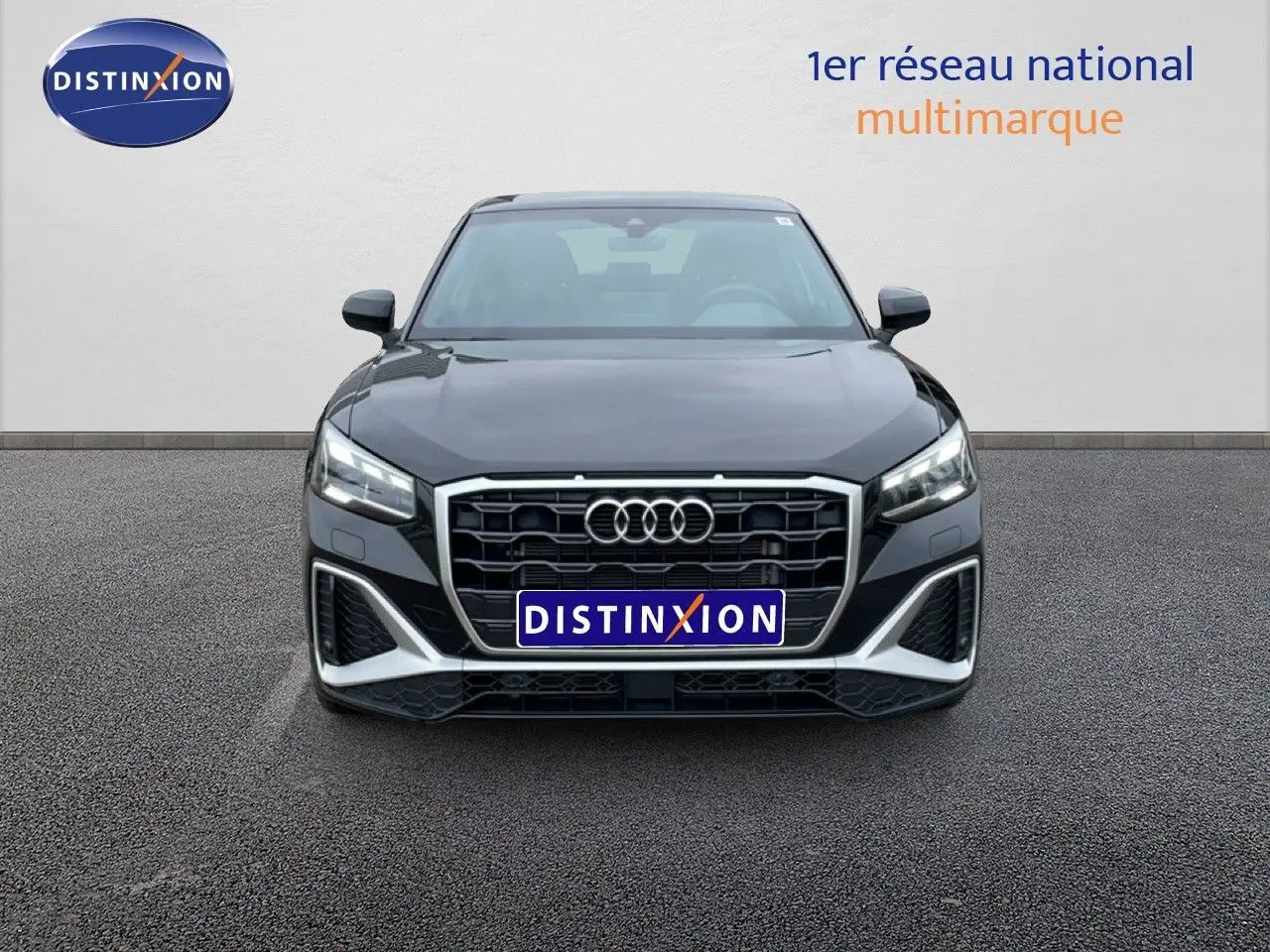 Vue frontale d'un Audi Q2 noir mito metal avec calandre hexagonale et phares LED allumés sur parking.