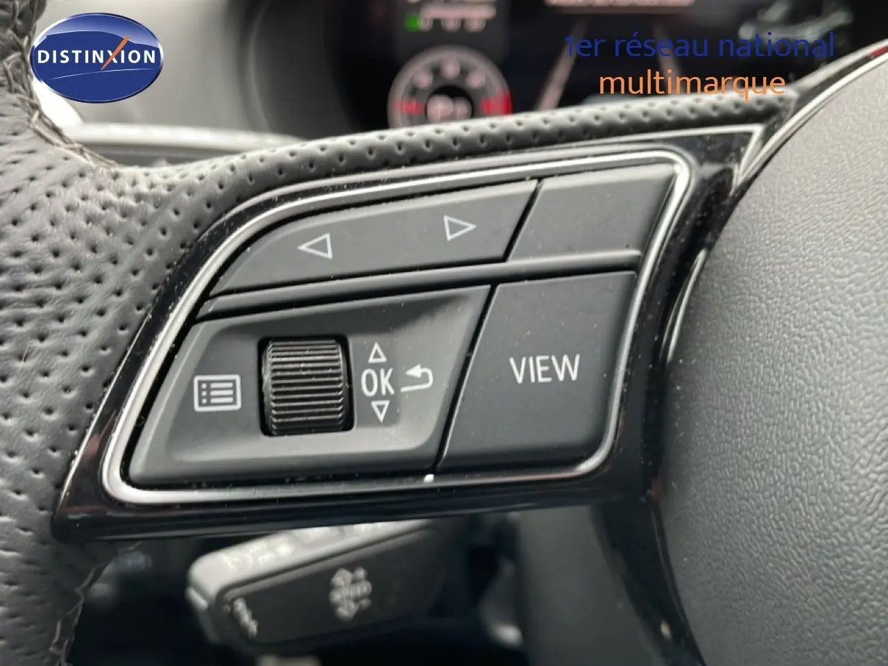 Gros plan sur les commandes gauche du volant perforé d’un Audi Q2 noir, avec boutons directionnels et fonction View.