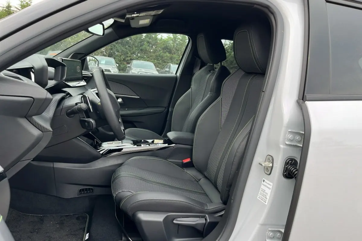 Vue intérieure côté conducteur du Peugeot 2008 Hybrid 145 GT Vision blanc okénite, sièges cuir tissu noirs avec surpiqûres vertes.