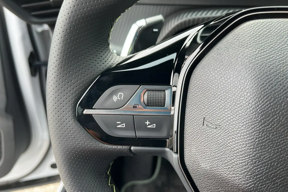 Gros plan sur le côté gauche du volant cuir perforé de la Peugeot 2008 Hybrid 145 avec commandes multifonctions.