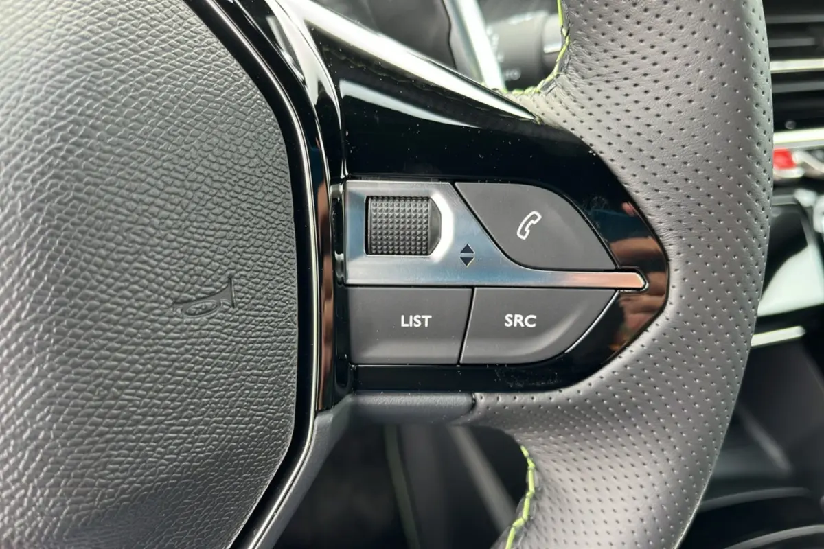 Gros plan sur les commandes gauche du volant cuir perforé de la Peugeot 2008 Hybrid 145 GT Vision 2025.