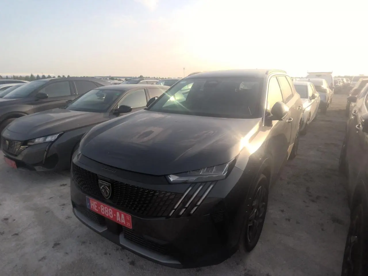 PEUGEOT 5008 gris foncé vue 3/4 avant droit, avec calandre noire et phares LED distinctifs au soleil couchant.