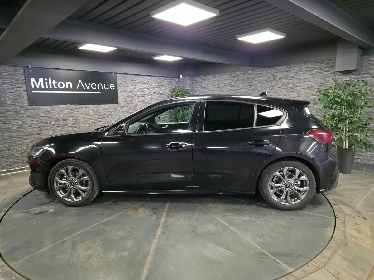 Vue de profil côté gauche d'une Ford Focus noire 2024 ST Line avec jantes alliage 17 pouces dans un showroom.
