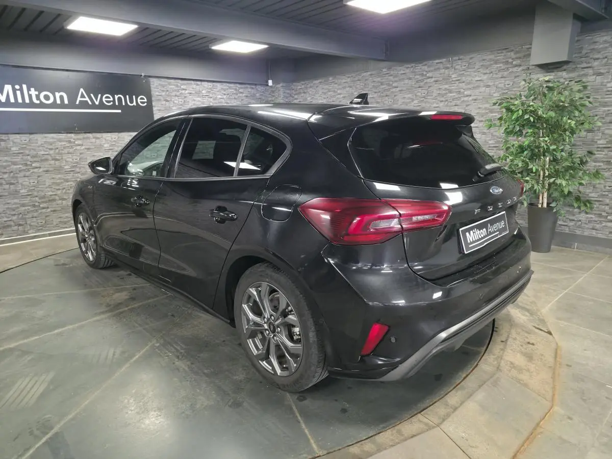 Ford Focus noire 2024 vue 3/4 arrière droit, jantes alliage 17'' et feux arrière LED dans un showroom.