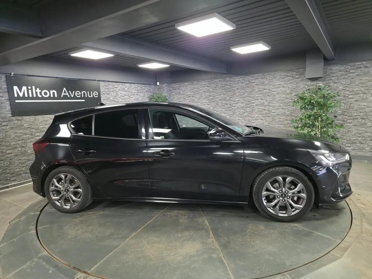 Vue de profil côté gauche d'une Ford Focus noire 2024 ST Line avec jantes alliage 17 pouces en intérieur showroom.