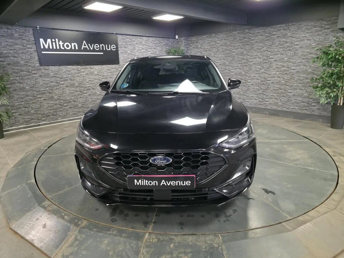 Vue avant d'une Ford Focus noire 2024 avec calandre noire hexagonale et badge ST-Line visible en intérieur showroom.