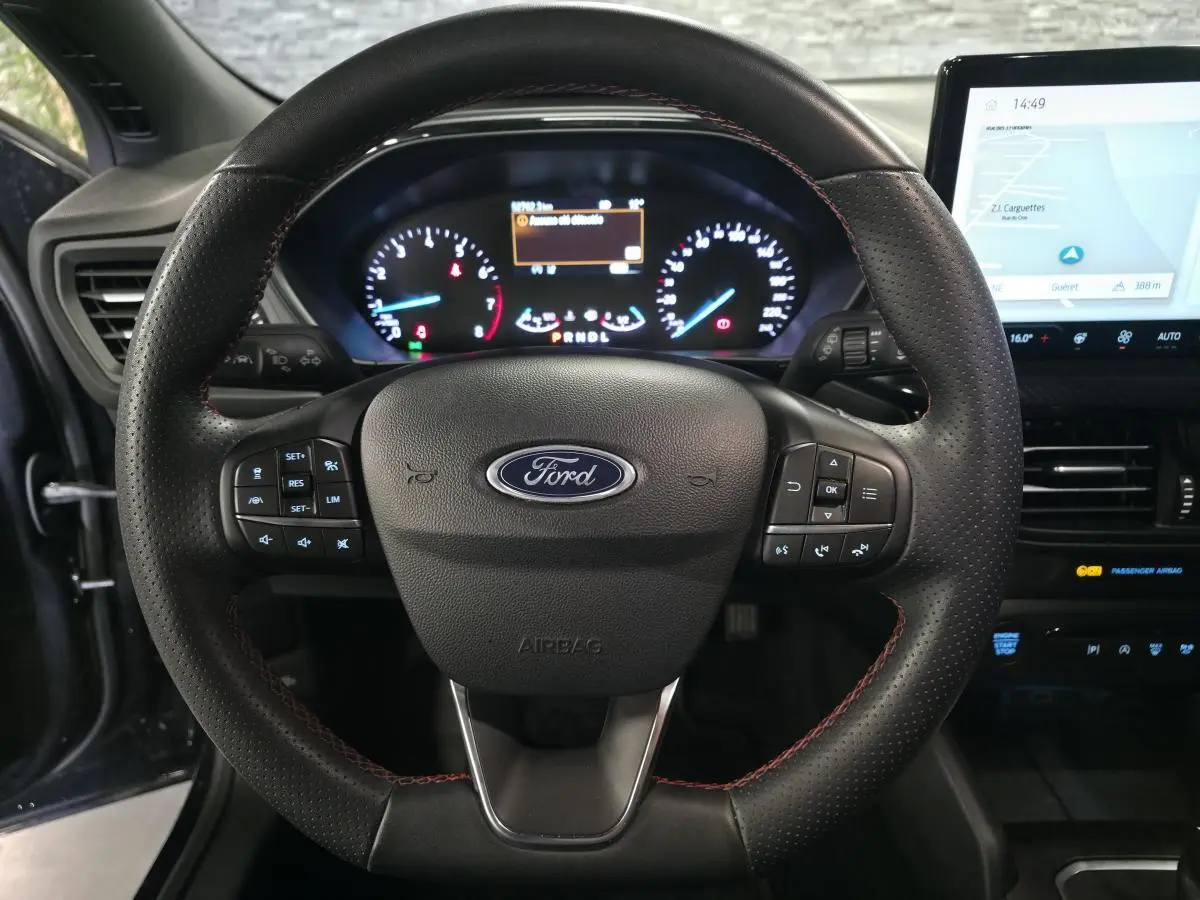 Vue intérieure centrée sur le volant ST Line en cuir noir avec surpiqûres rouges et tableau de bord numérique Ford Focus 2024.