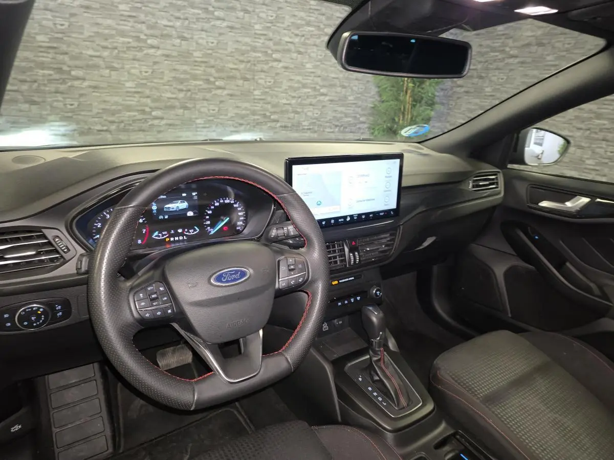 Vue intérieure avant droite de la Ford Focus 2024, volant ST Line noir avec surpiqûres rouges et écran tactile central.