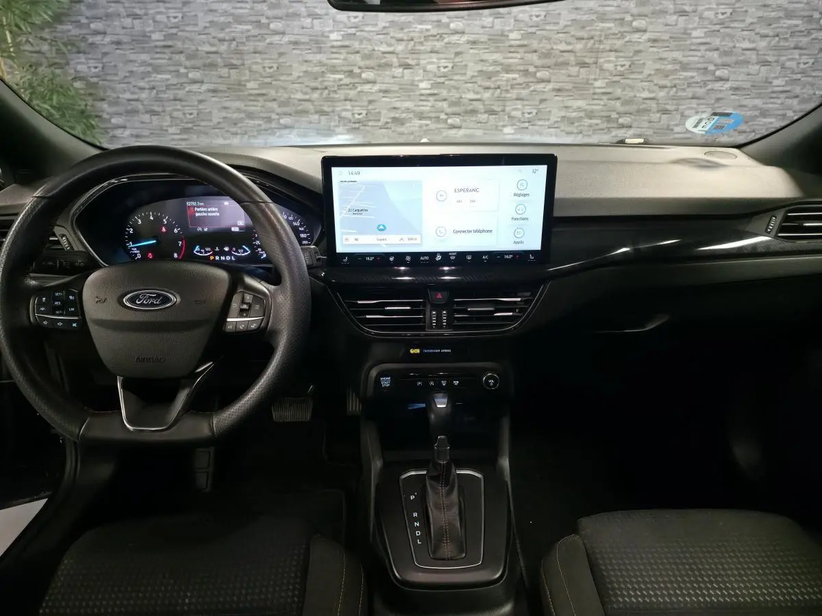 Vue intérieure avant de la Ford Focus 2024 noire, tableau de bord avec écran tactile central et volant multifonction.