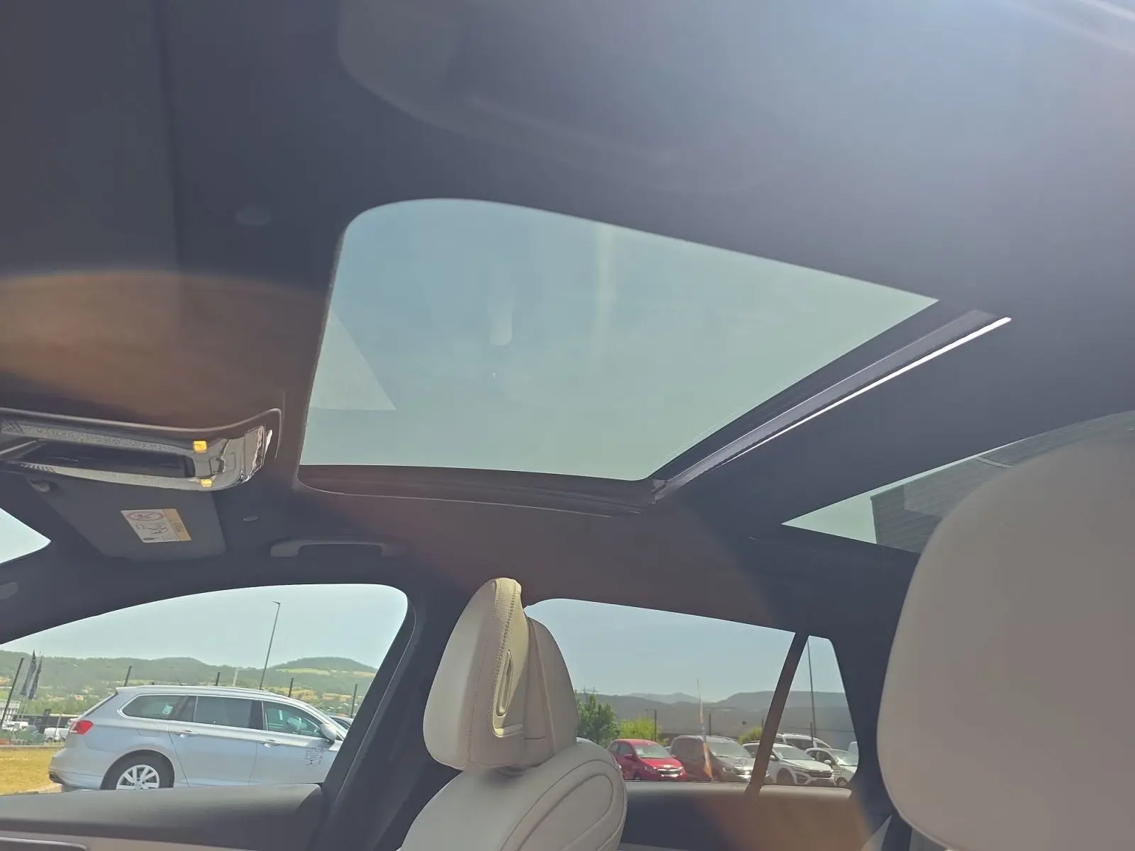 Vue intérieure du toit ouvrant panoramique et des sièges avant en cuir clair d’un break Mercedes Classe C gris foncé.