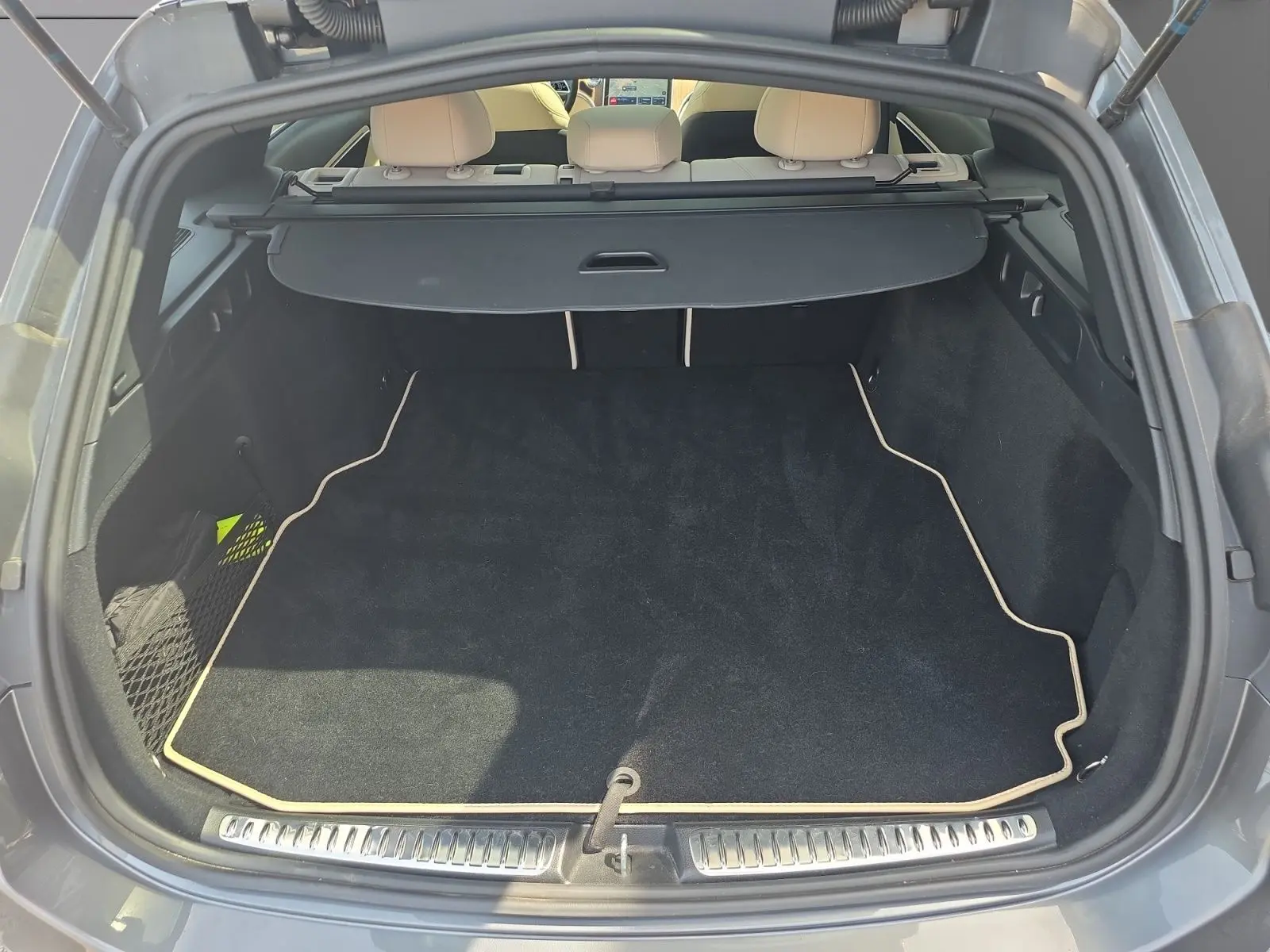 Vue arrière du coffre ouvert d’un Mercedes Classe C Break gris foncé, avec tapis noir et cache-bagages déployé.