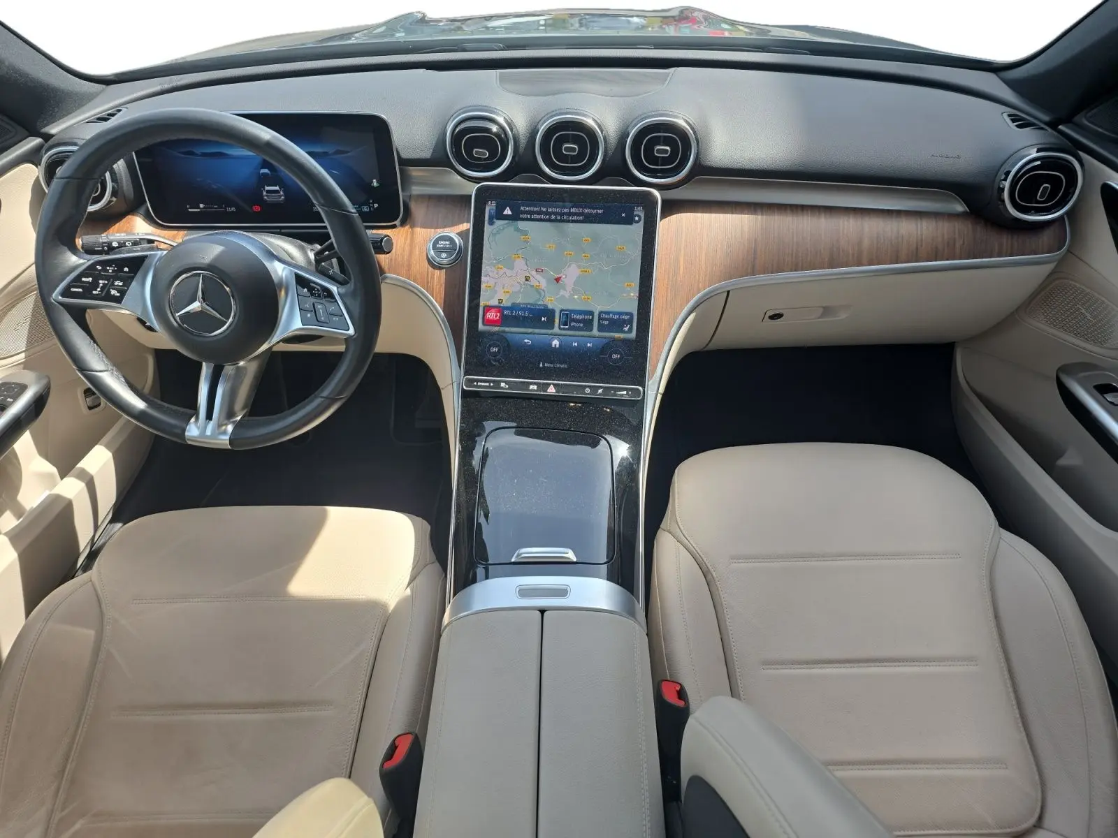 Vue intérieure avant du Mercedes Classe C Break 220 D 4MATIC avec sellerie cuir beige et tableau de bord bois et écran tactile central.
