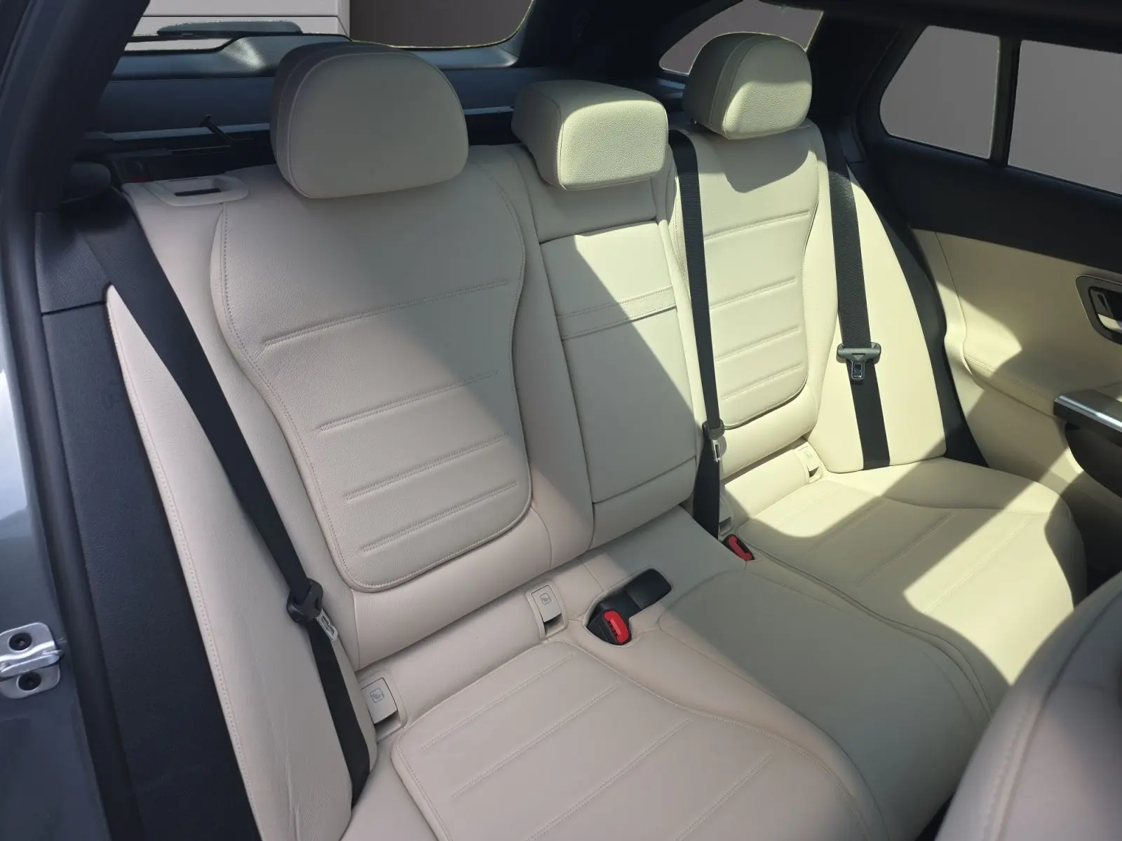 Vue intérieure des sièges arrière en cuir beige clair d’un Mercedes Classe C Break gris foncé, avec ceinture de sécurité noire.
