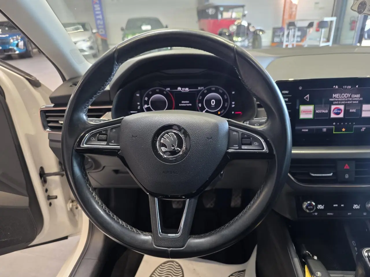 Vue frontale centrée sur le volant cuir noir de la Skoda Scala blanche, avec tableau de bord digital et écran tactile visible.