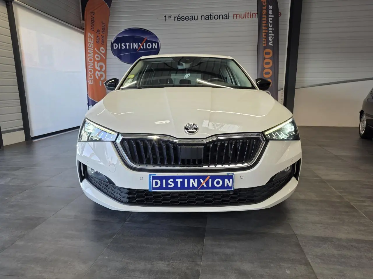 Vue frontale d'une Skoda Scala blanche avec calandre noire et phares LED allumés en intérieur showroom.
