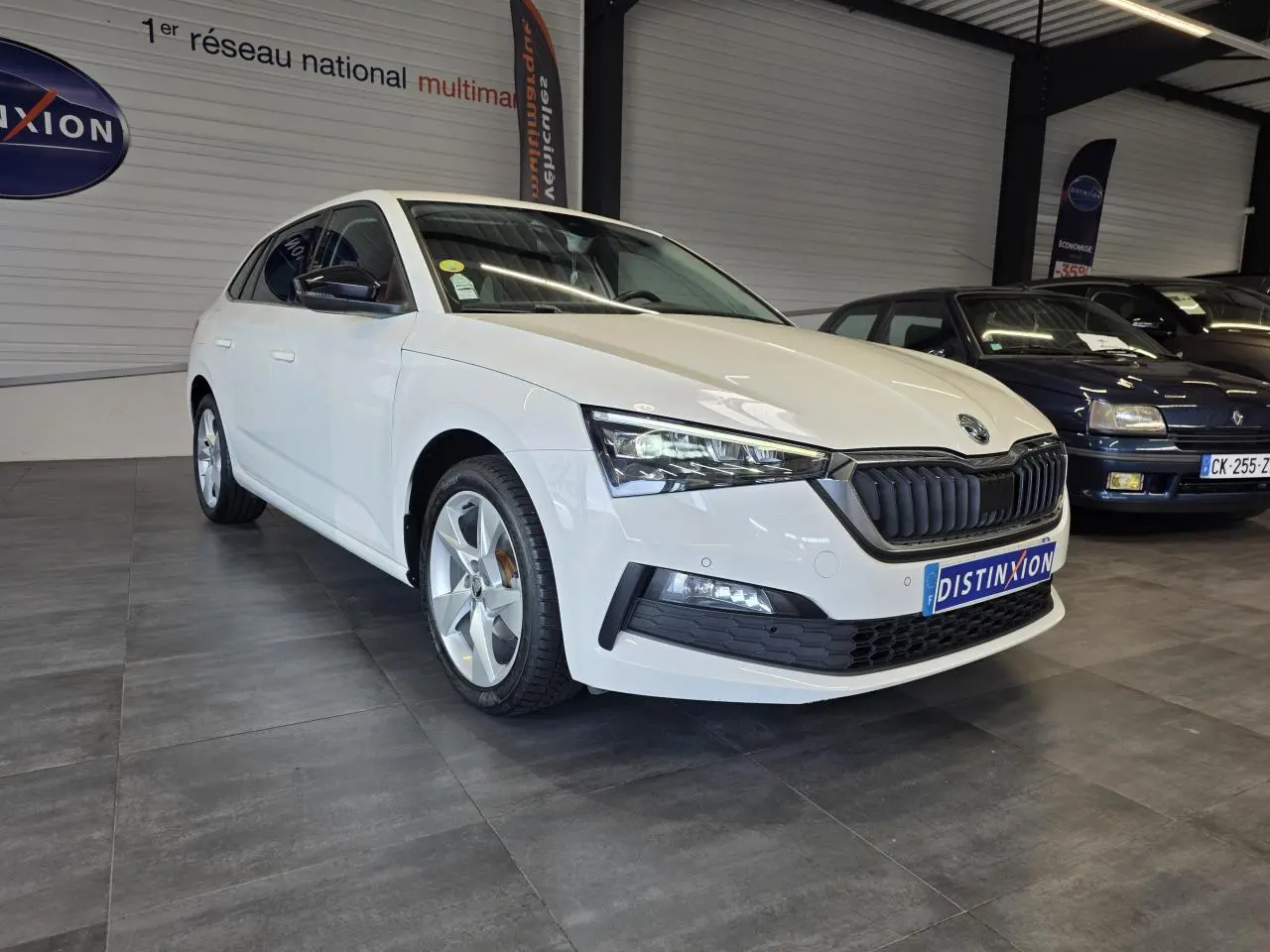 Vue 3/4 avant droite d'une Skoda Scala blanche avec calandre noire et jantes alliage argent dans un showroom.