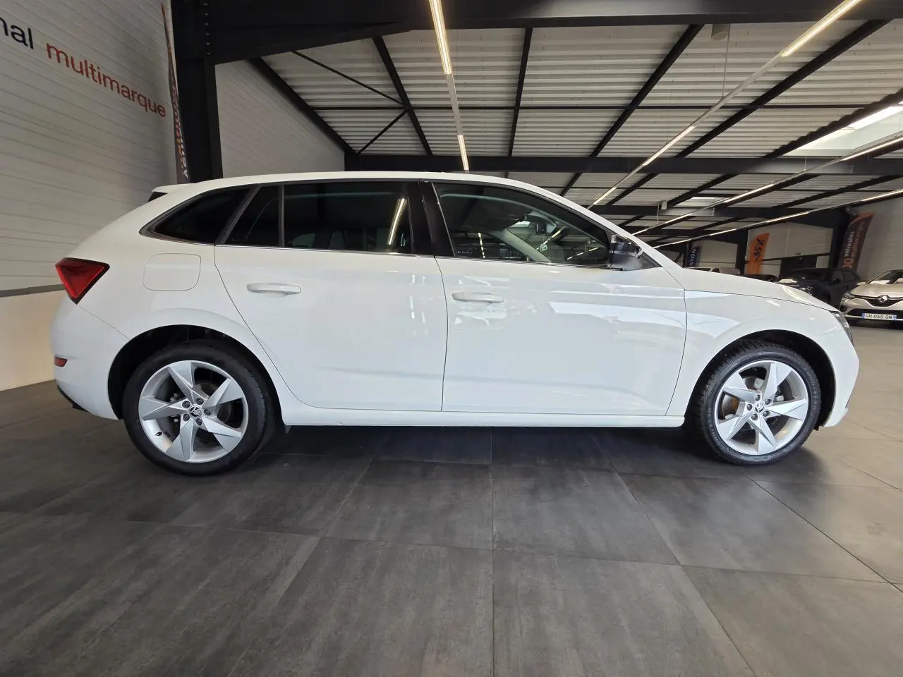Vue latérale droite d'une Skoda Scala blanche 2020 en showroom, avec jantes alliage argent et vitres teintées.